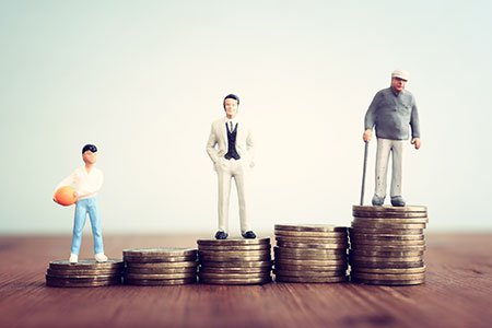 stack of coins increasing in size starting with young person at one end middleaged man in the middle and senior at the end