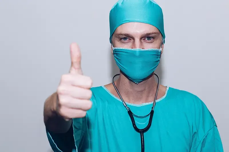 surgeon wearing a mask and stethoscope giving a thumbs up.webp