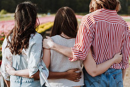 three female friends with with their arms around each others backs in support