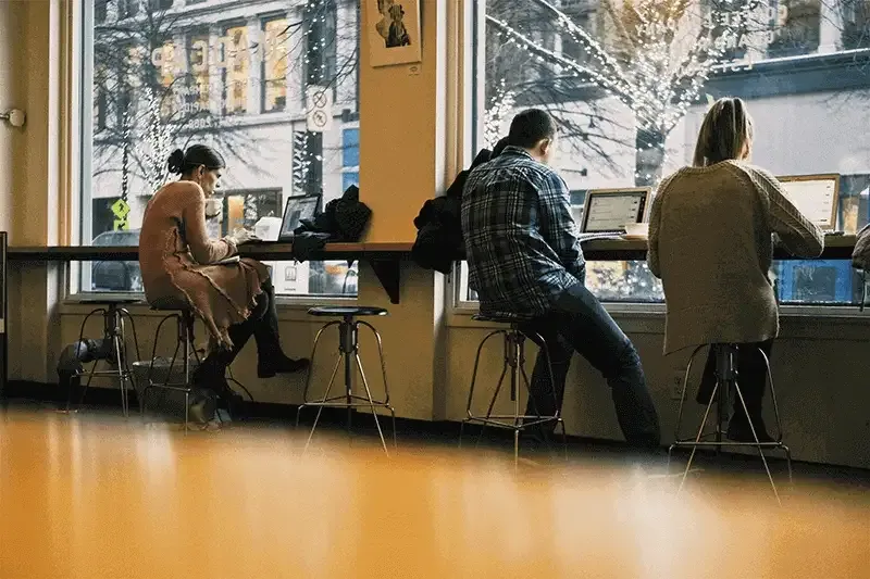 three-people-sitting-on-stools-at-a-cafe-working-on-their-laptops