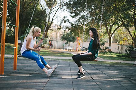 two women sitting on swings at the park talking and laughing