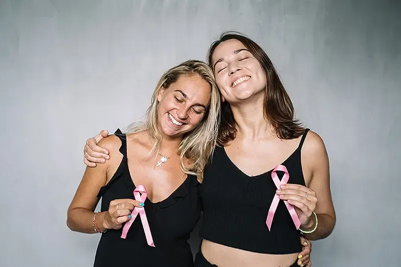 two women hugging holding breast cancer awareness ribbons