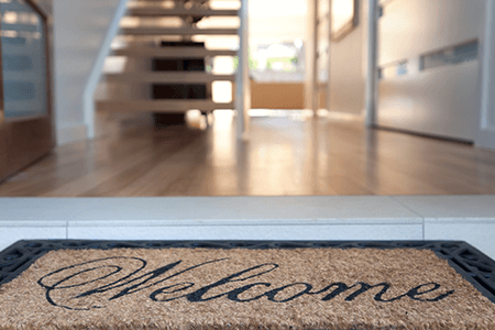 welcome-mat-at-an-open-front-door-exposing-hallway-and-staircase