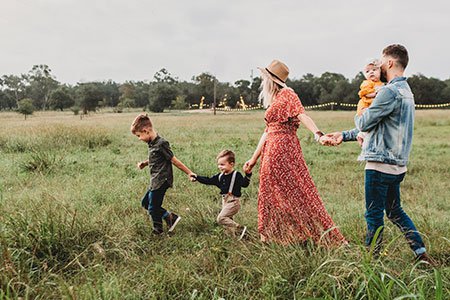 woman holding hands with two children and man holding baby in field