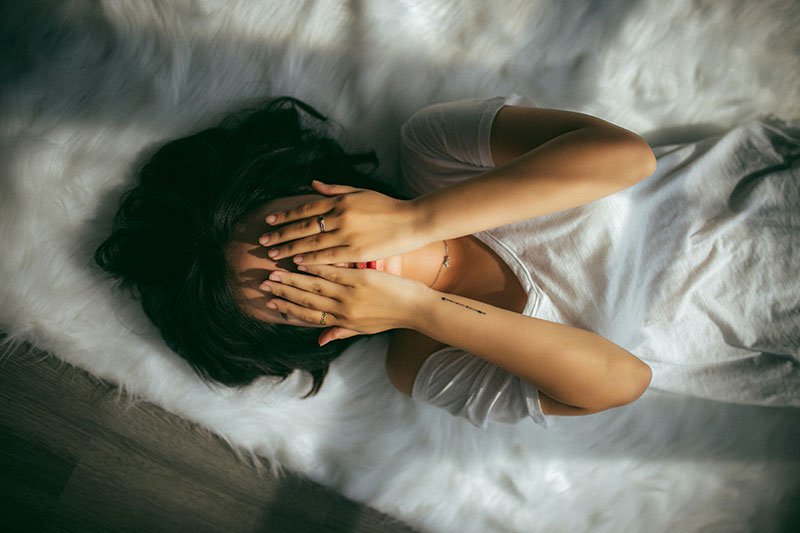 woman lying on the floor with her hands covering her face