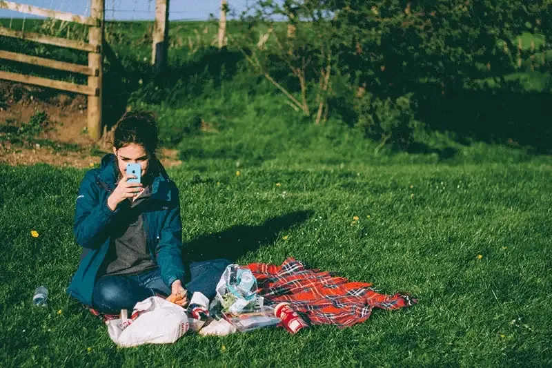 woman-sitting-on-a-picnic-rug-on-the-grass-using-smartphone-for-a-video-call