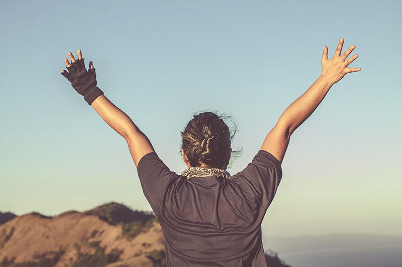 Woman standing on top of a hill with her arms stretched out in the air