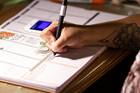 woman with tattoo writing in planner - listing