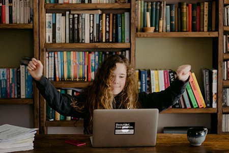 young-girl-at-home-doing-school-work-on-her-laptop-with-arms-raised-in-the-air