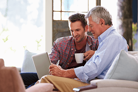 young-man-drinking-coffee-with-older-man-both-looking-at-a-laptop-screen